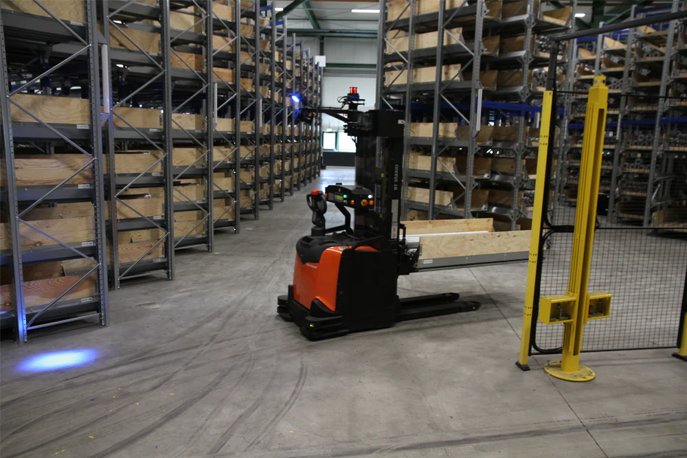 De foto toont een heftruck die rijdt tussen de inrijstellingen met een kist vol lange buizen
