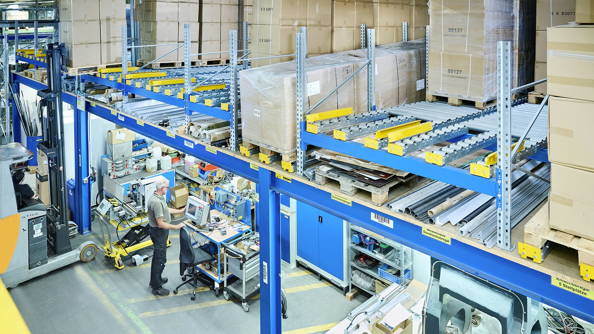 Zwei Mitarbeiter in einer Werkstatt. Über ihnen befindet sich ein Palettendurchlaufregal von BITO