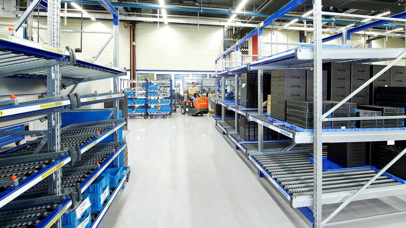 Ein Mann auf einem Flurförderzeug zwischen Durchlaufregalen.