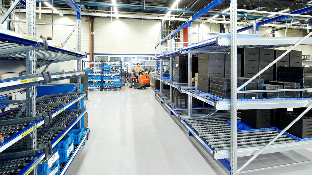 Ein Mann auf einem Flurförderzeug zwischen Durchlaufregalen.