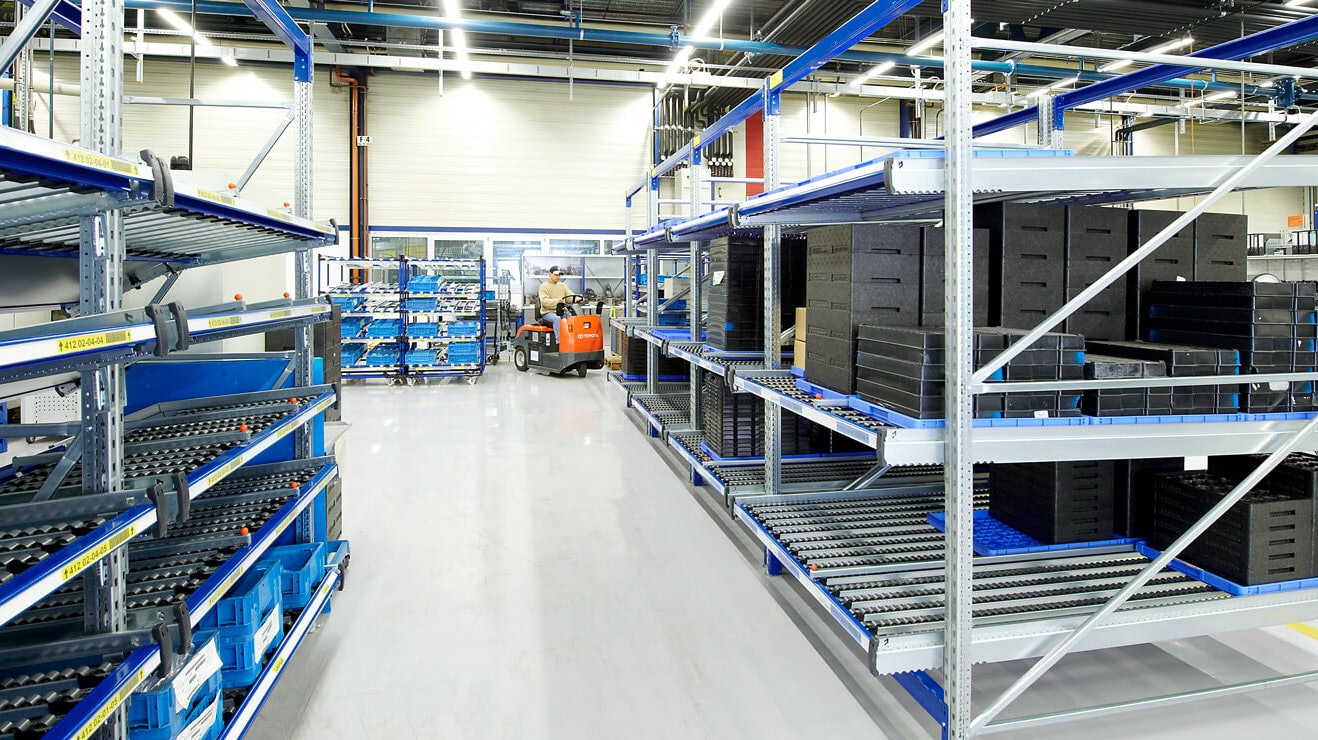 Ein Mann auf einem Flurförderzeug zwischen Durchlaufregalen.