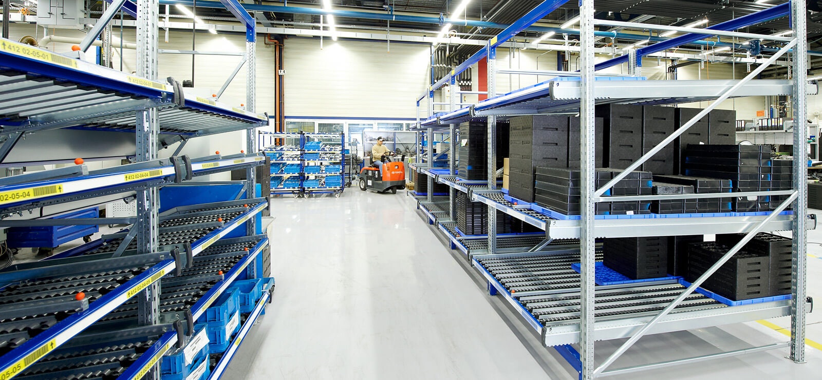 Ein Mann auf einem Flurförderzeug zwischen Durchlaufregalen.