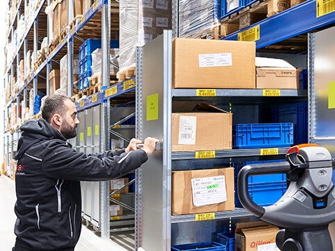 Ein Mann der einen Rollwagen unter ein Palettenregal fährt