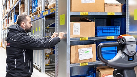 Ein Mann der einen Rollwagen unter ein Palettenregal fährt