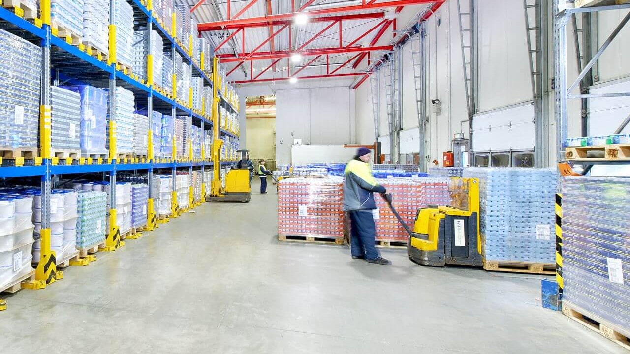 Drei Männer auf Flurförderzeugen an einem Palettendurchlaufregal