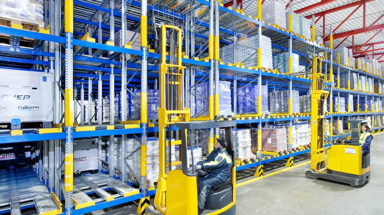 Zwei Arbeiter auf Flurförderzeugen an einem Palettendurchlaufregal
