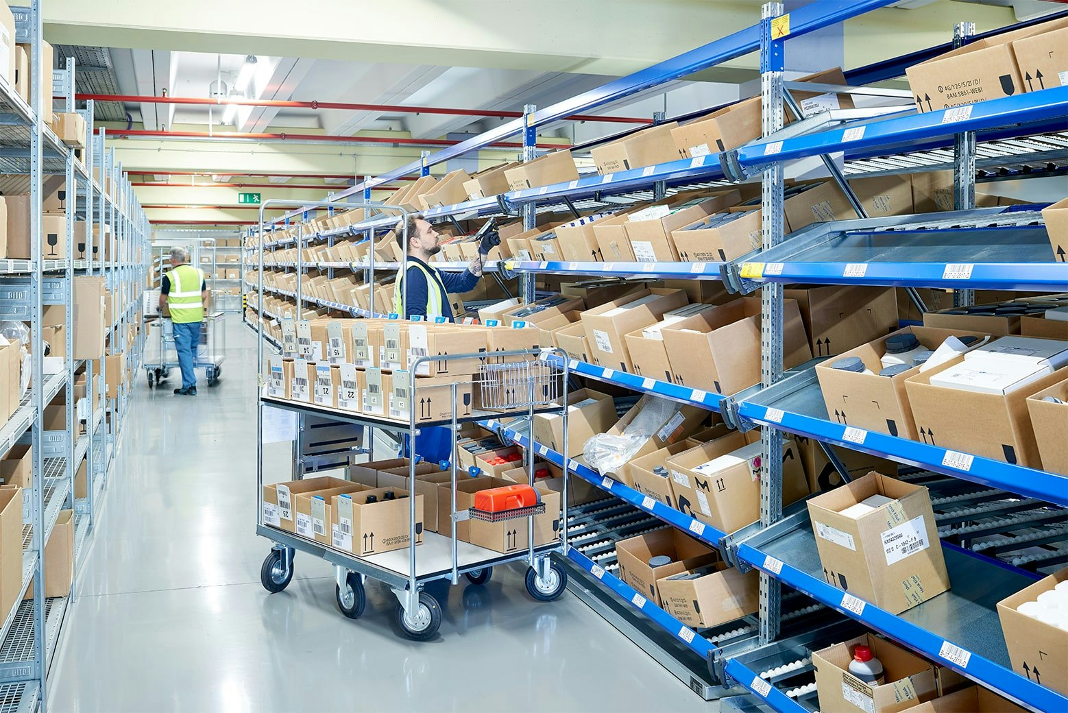 Zwei Mitarbeiter an BITO Durchlaufregalen mit Schrägböden und an einem Fachbodenregal