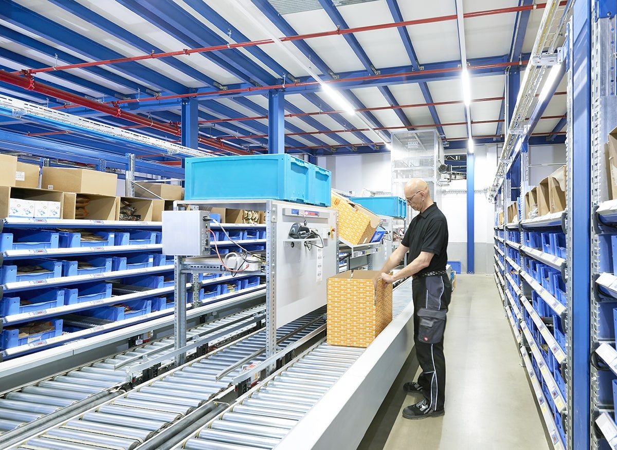 Ein Lagerarbeiter an einer Fördertechnik zwischen BITO Durchlaufregalen