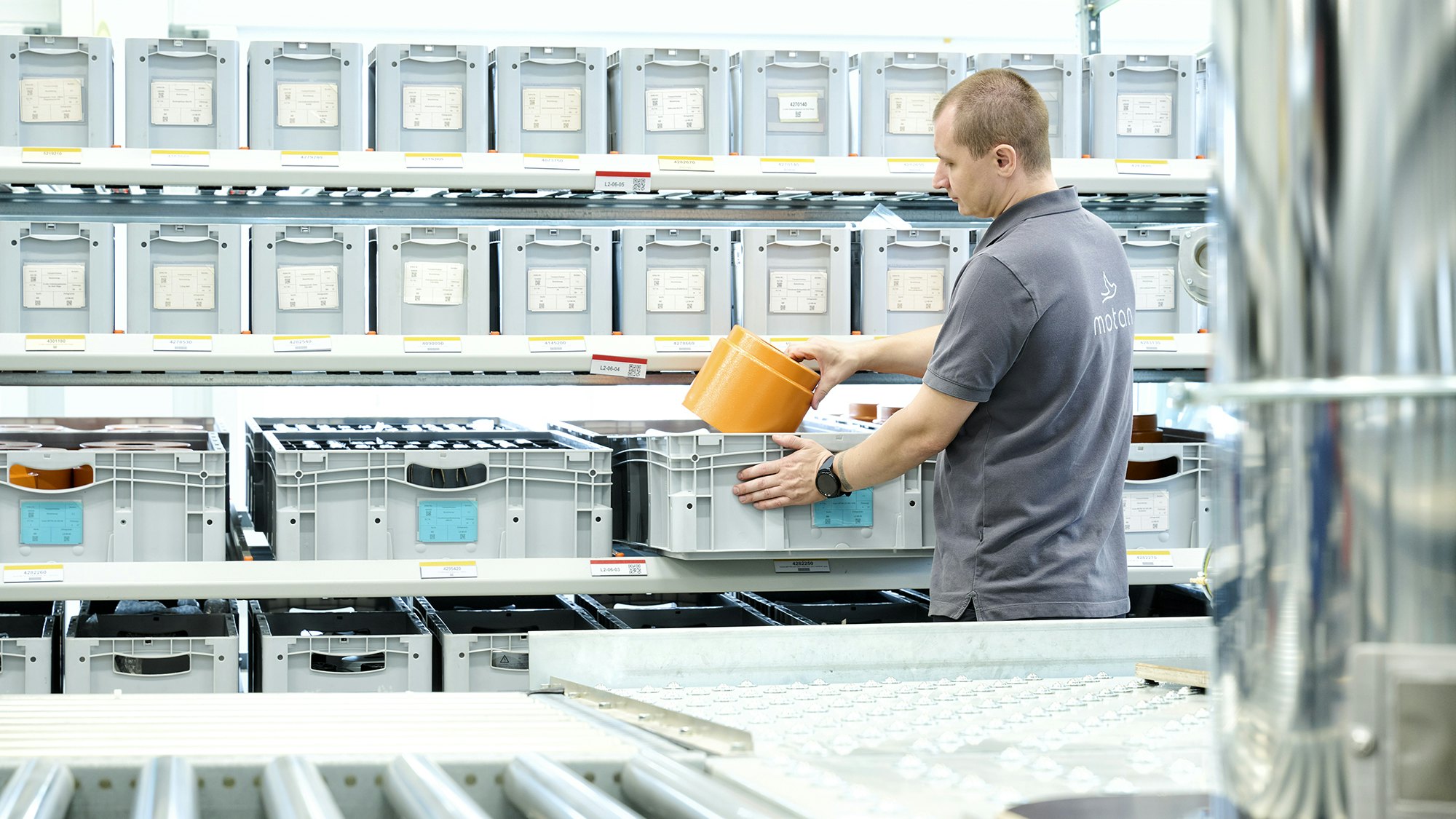 Mitarbeiter kommissioniert Bauteile aus Lagerbehältern am Durchlaufregal von BITO.