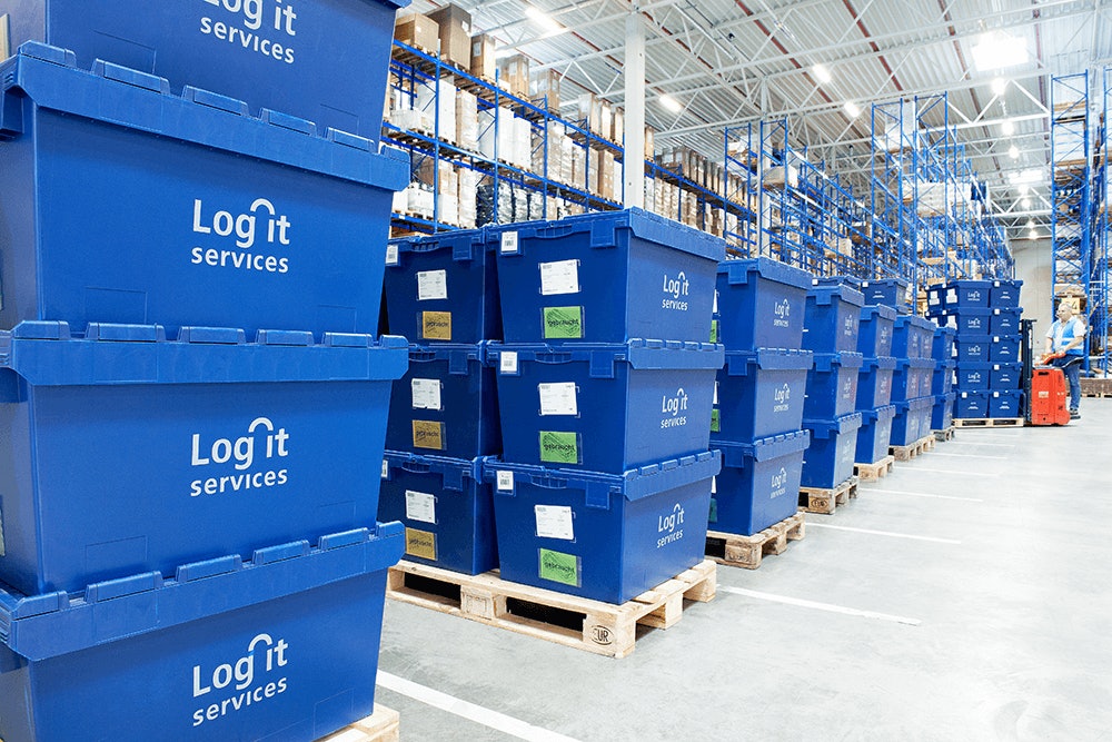 Kisten auf Paletten gestapelt stehen vor einem großen Lagerregal in einer Lagerhalle.