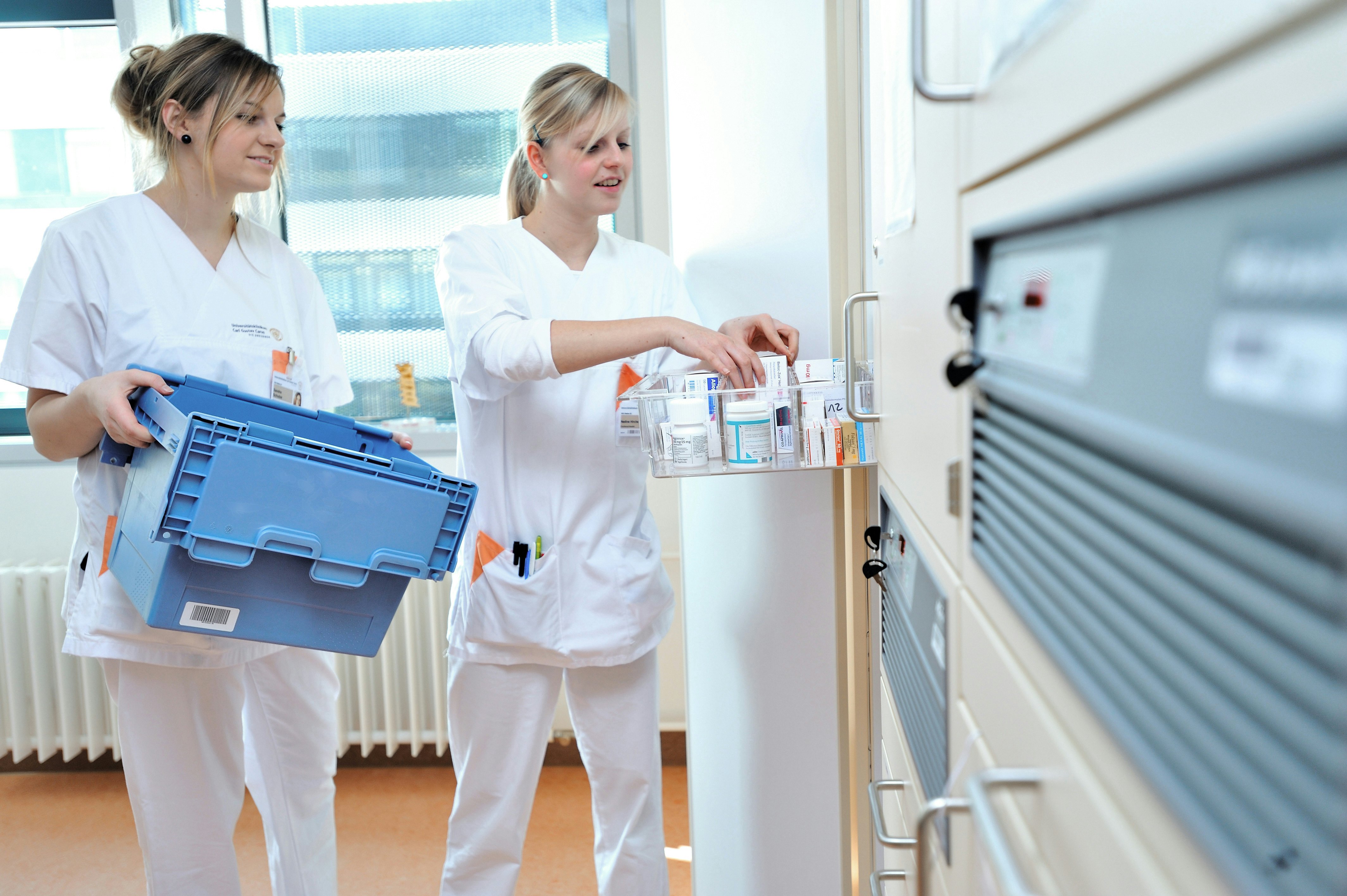 Zwei Angestellte eines Pharmakonzerns räumen Medikamente aus einem Mehrwegbehälter in eine Schublade