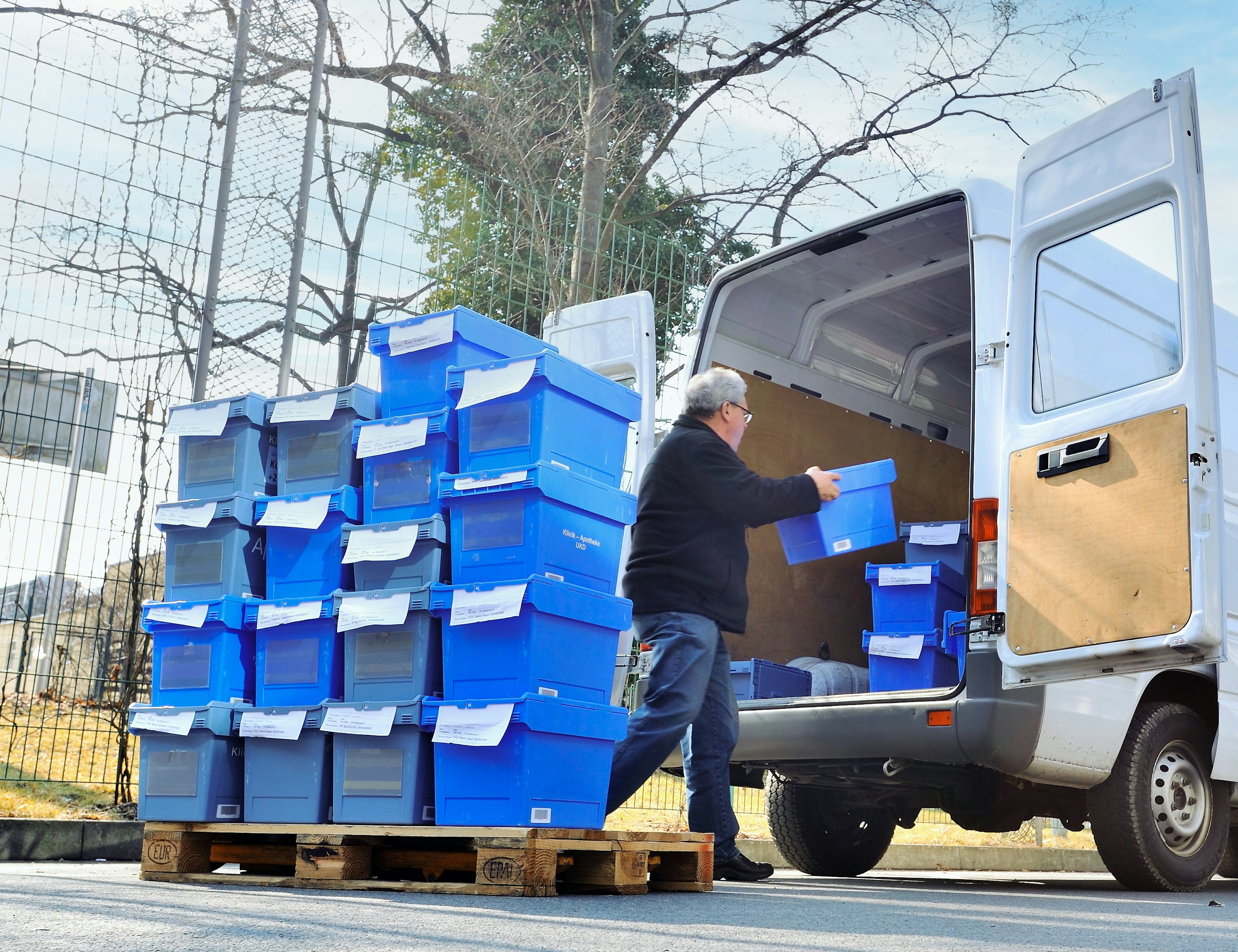 Ein Mann lädt BITO Behälter für die Apotheke von einer Palette in einen kleinen Bus ein.