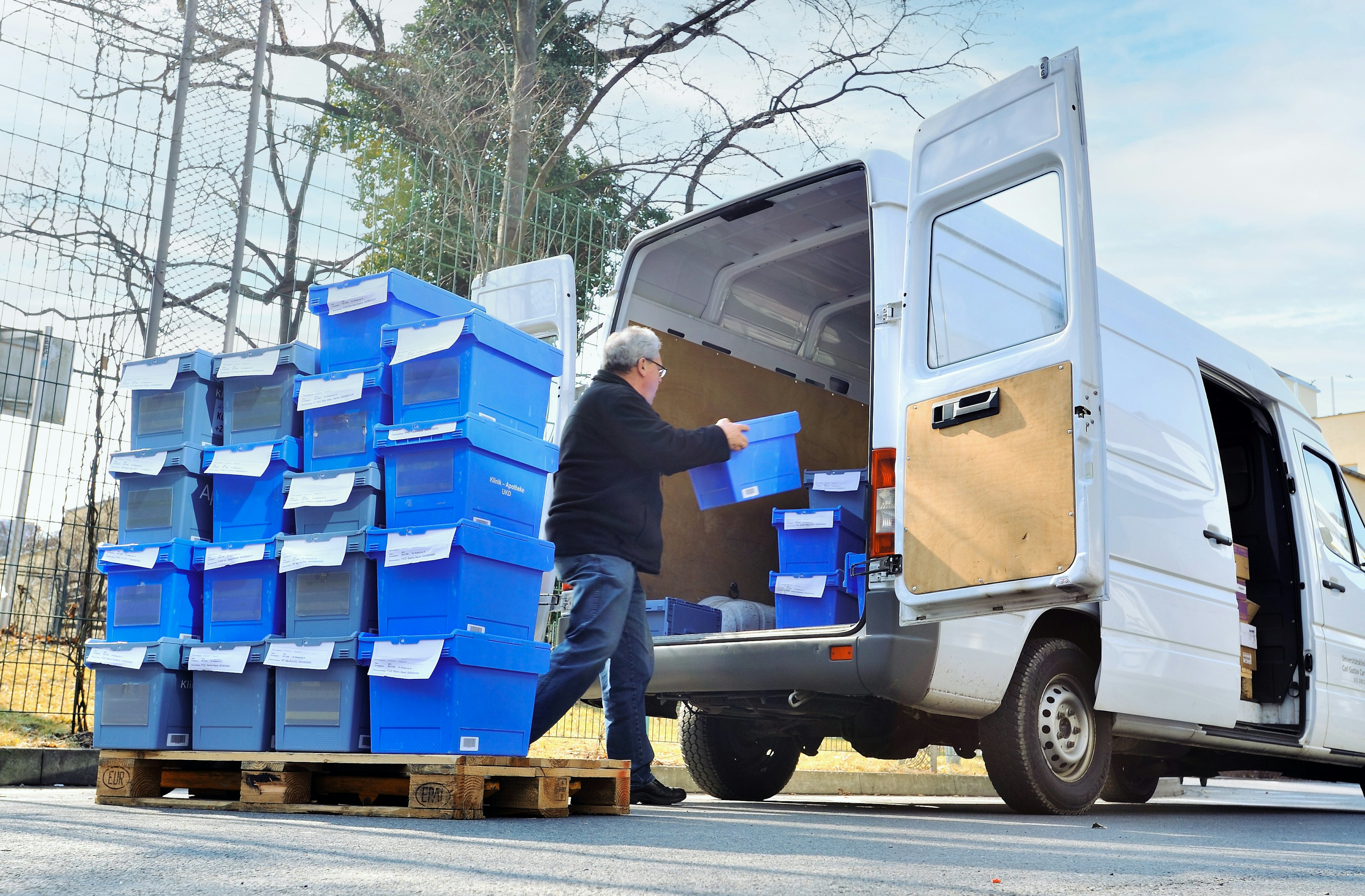 Ein Mann lädt BITO Behälter für die Apotheke von einer Palette in einen kleinen Bus ein.