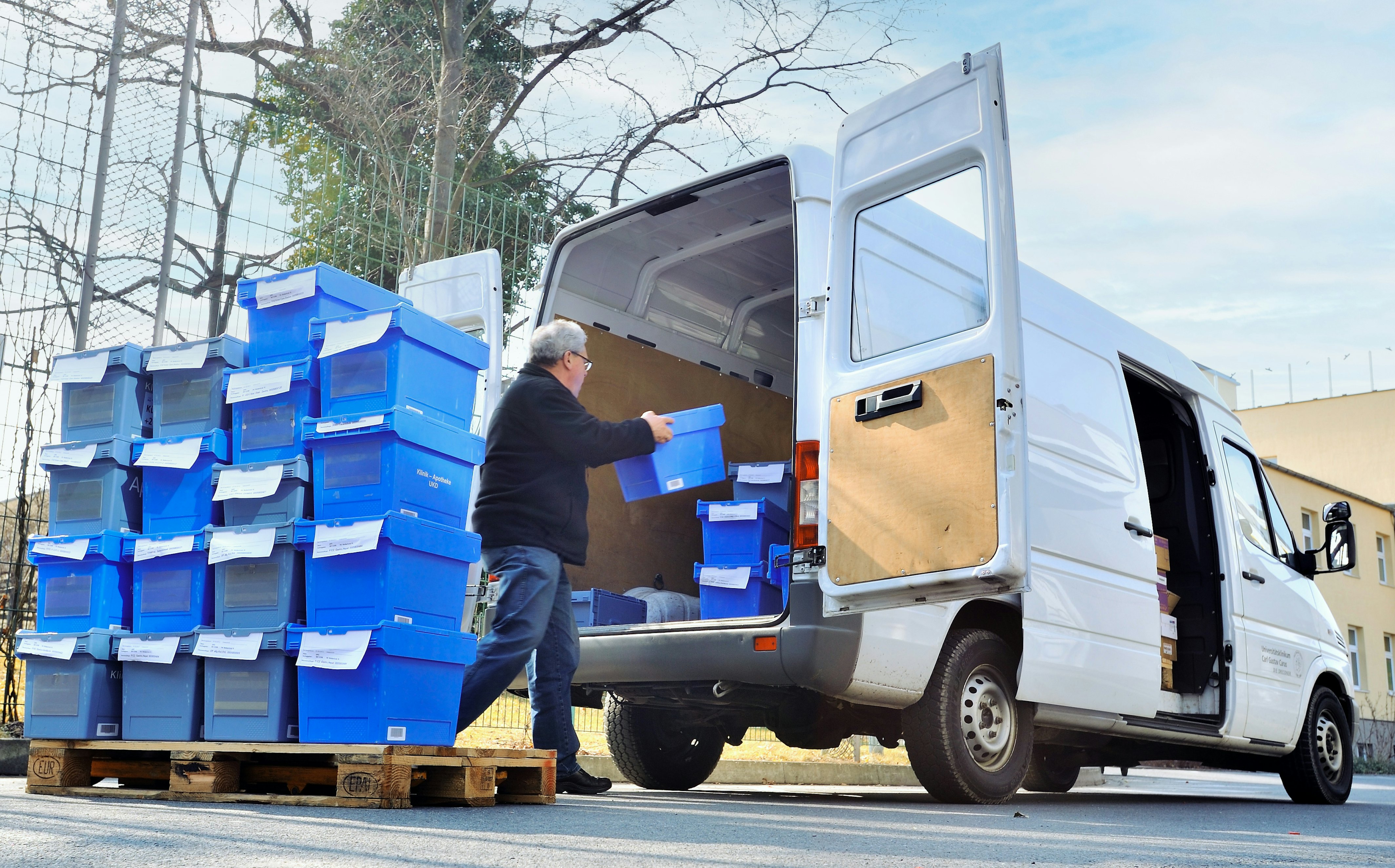 Ein Mann lädt BITO Behälter für die Apotheke von einer Palette in einen kleinen Bus ein.