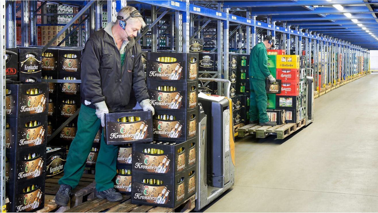 BITO Paletten-Durchlaufregal-System Getränkekisten werden in einem BITO Palettendurchlaufregal gelagert. Zwei Mitarbeiter setzen die Kisten aus dem Regal auf den Stapler.