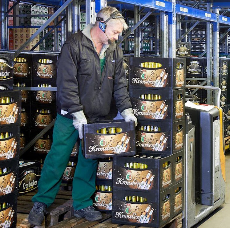 Pallegennemløbsreoler Getränkekisten werden in einem BITO Palettendurchlaufregal gelagert. Zwei Mitarbeiter setzen die Kisten aus dem Regal auf den Stapler.