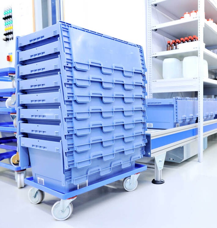 Pojemniki transportowe MB Gestapelte BITO Behälter stehen in einem Lager der Apotheke. Dort befindet sich ebenfalls ein BITO Regal mit Medikamenten und Rollleisten auf denen ebenfalls BITO Behälter stehen.