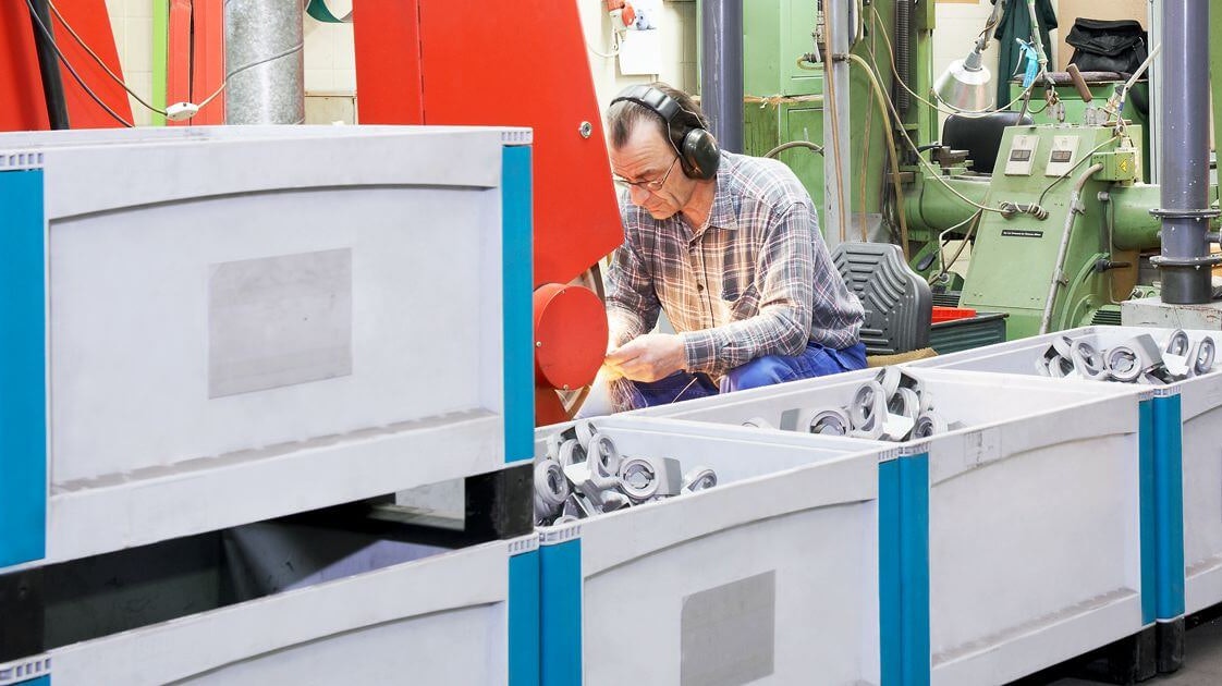 Pojemniki na duże obciążenia SL Arbeiter von Schubert und Salzer Maschinenbau arbeiten an Maschinen. Die bereits fertigen Produkte werden in BITO Behältern gelagert.