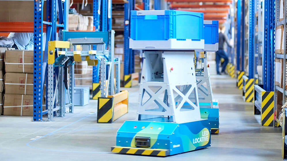 BITO LEO Ein LEO Locative fährt auf seiner Spur zwischen BITO Regalen in Richtung Übergabestation. Er transportiert einen BITO Behälter.