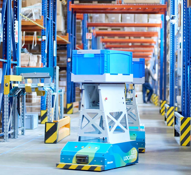 BITO LEO Ein LEO Locative fährt auf seiner Spur zwischen BITO Regalen in Richtung Übergabestation. Er transportiert einen BITO Behälter.