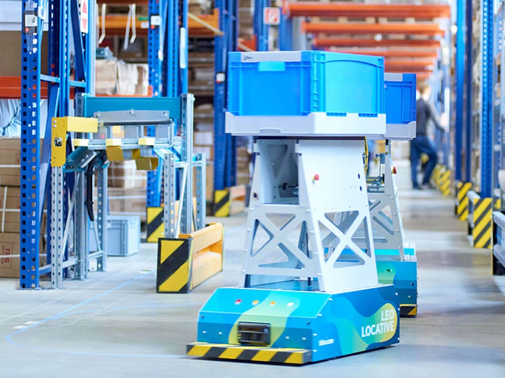 BITO LEO Ein LEO Locative fährt auf seiner Spur zwischen BITO Regalen in Richtung Übergabestation. Er transportiert einen BITO Behälter.