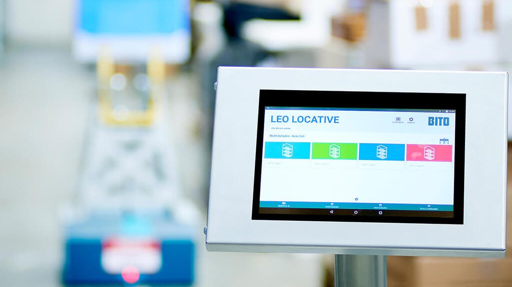 BITO LEO App Das Tablet zum Steuern vom LEO Locative steht im Vordergrund. Dahinter sieht man einen LEO fahren.