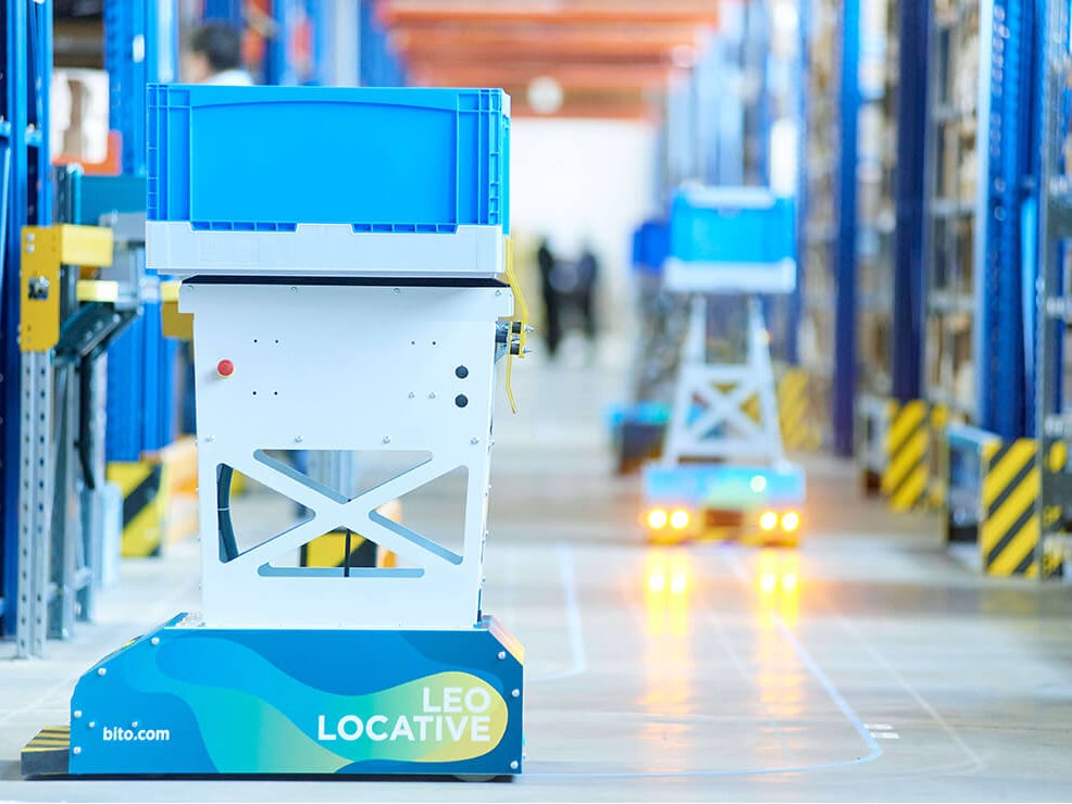 BITO LEO Der LEO Locative fährt auf seiner geklebten Spur zwischen BITO Regalen entlang. Er transportiert einen BITO Behälter.