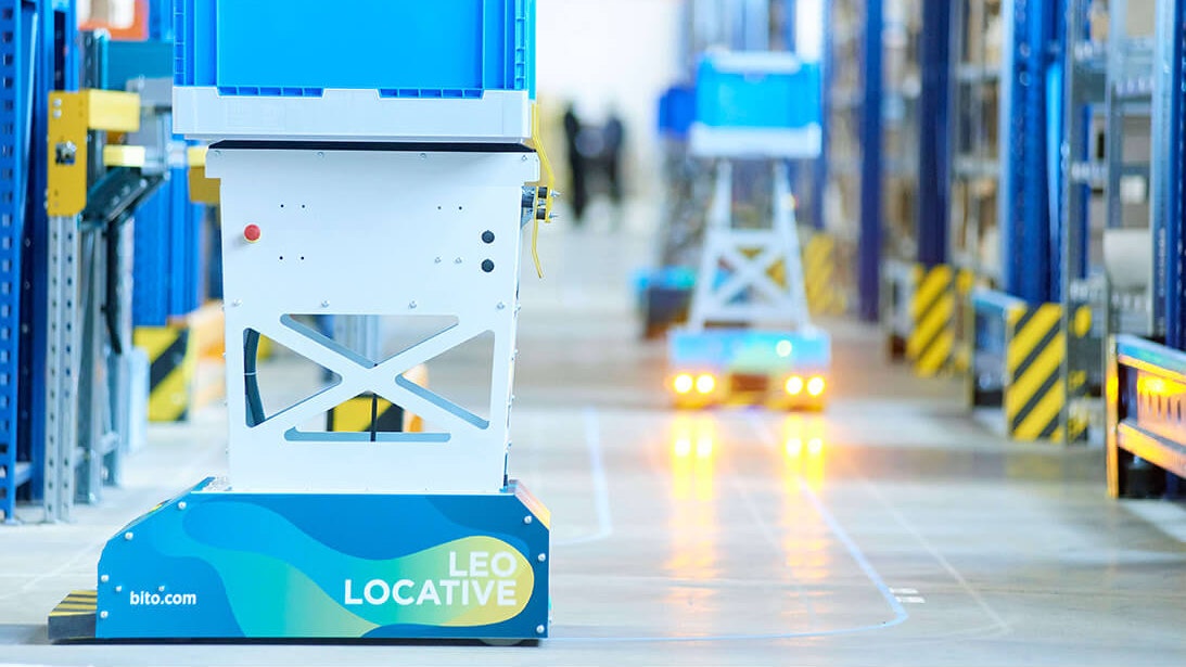 BITO LEO Der LEO Locative fährt auf seiner geklebten Spur zwischen BITO Regalen entlang. Er transportiert einen BITO Behälter.