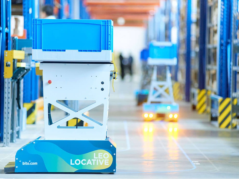 BITO LEO AGV Der LEO Locative fährt auf seiner geklebten Spur zwischen BITO Regalen entlang. Er transportiert einen BITO Behälter.