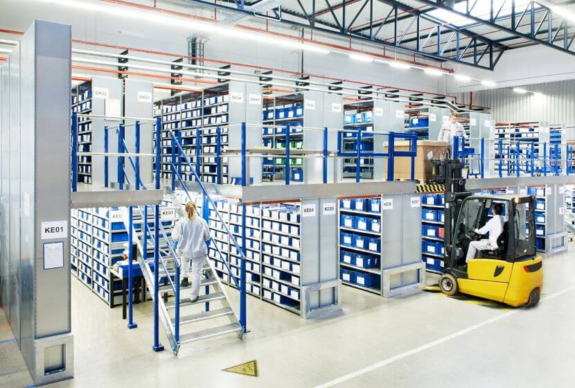 Estanterías multinivel de BITO Eine BITO Lagerlösung auf zwei Etagen. Eine Frau geht gerade die Treppe nach oben, während rechts von ihr ein Paket mit dem Stapler in die zweite Etage gelagert wird.