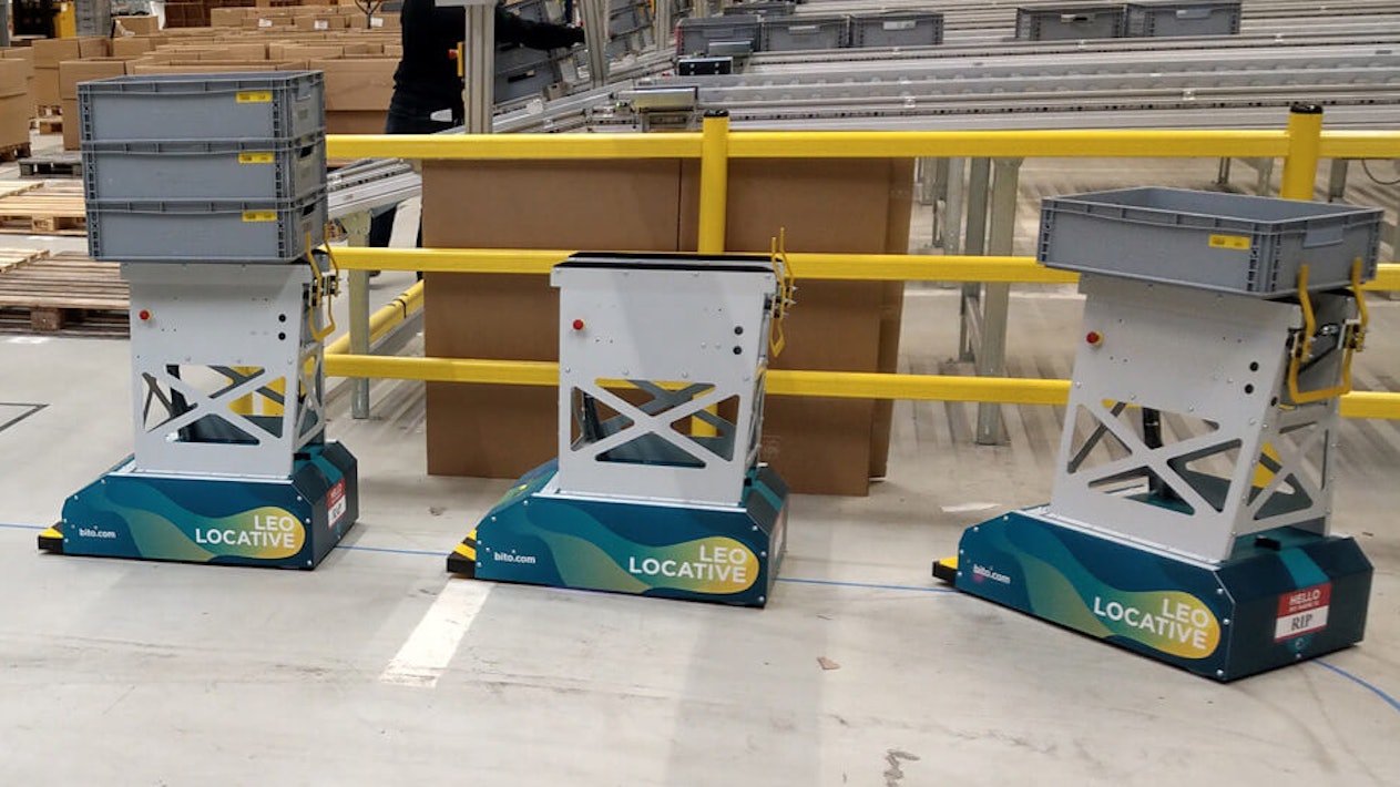 BITO LEO Drei LEO Locative fahren auf ihrer Bahn in einer Halle. Zwei davon sind mit Behälter beladen. Sie bewegen sich in Richtung der Übergabestation von BITO.