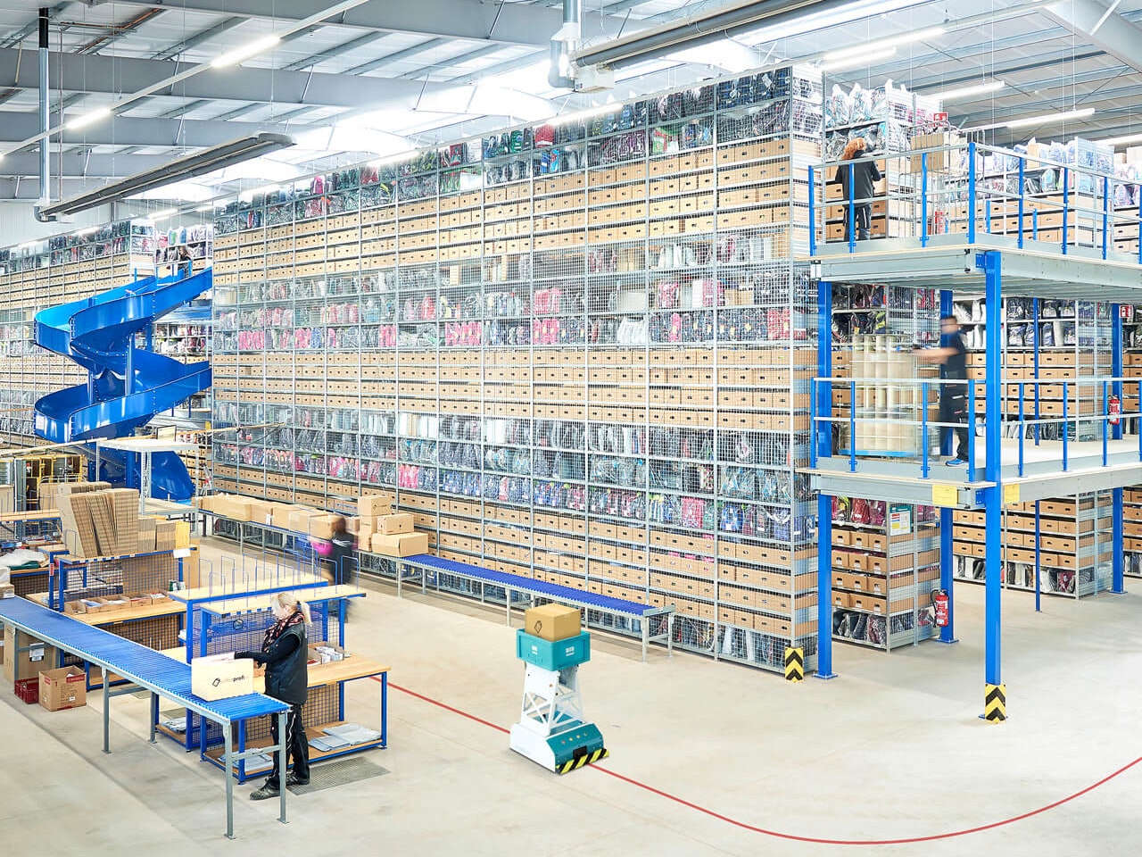 Wielopiętrowe instalacje regałowe, regały półkowe BITO i BITO LEO Eine BITO Mehrgeschossanlage, in der Schulranzen gelagert werden. Davor fährt ein LEO auf seiner Bahn, der ein Paket in einem BITO Behälter transportiert.