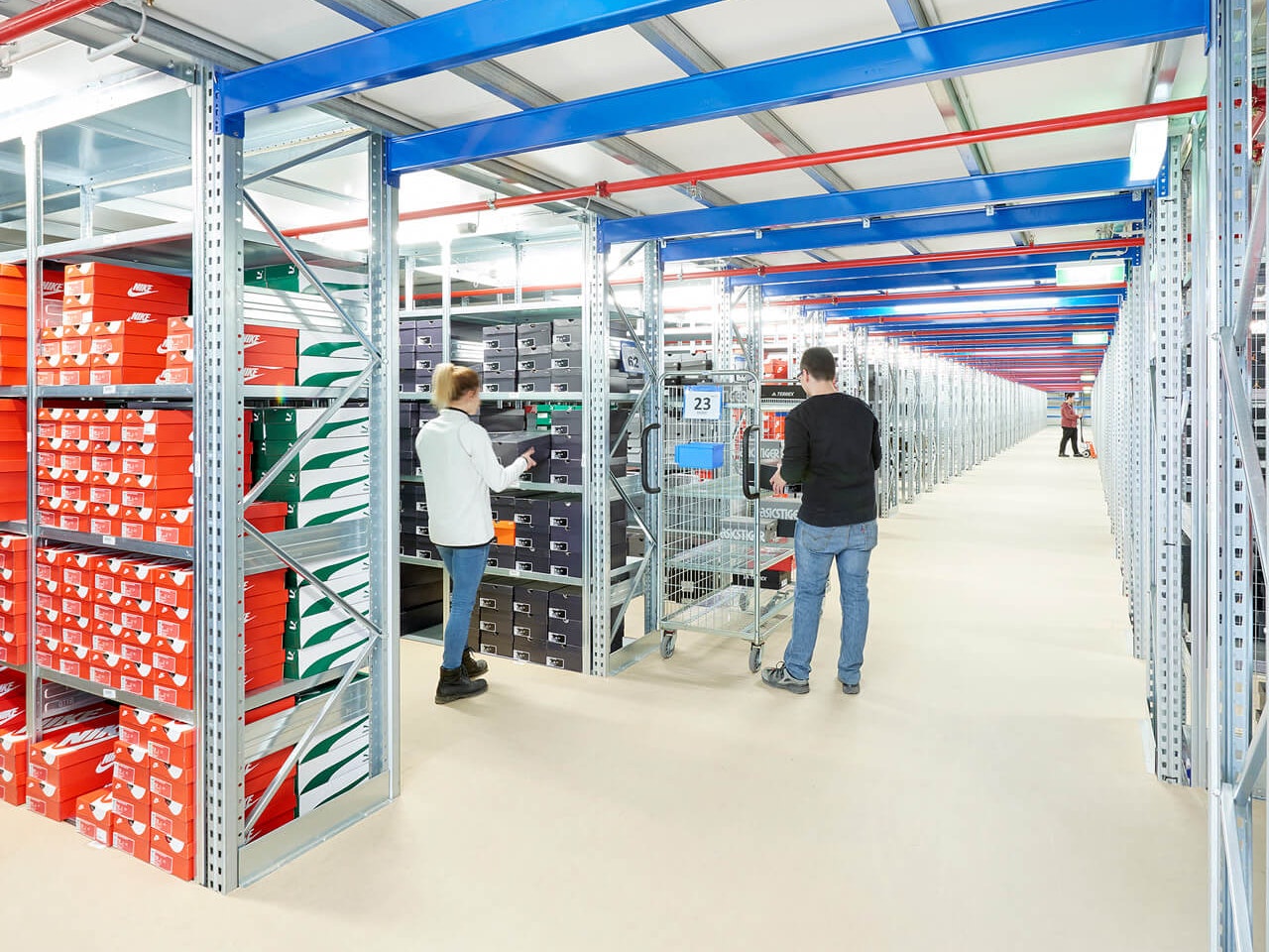 Wielopiętrowe instalacje regałowe i regały półkowe BITO Ein BITO Fachbodenregal, in dem Schuhkartons gelagert werden. Ein Mann lädt verschiedene Kartons aus dem Regal auf seinen Wagen.