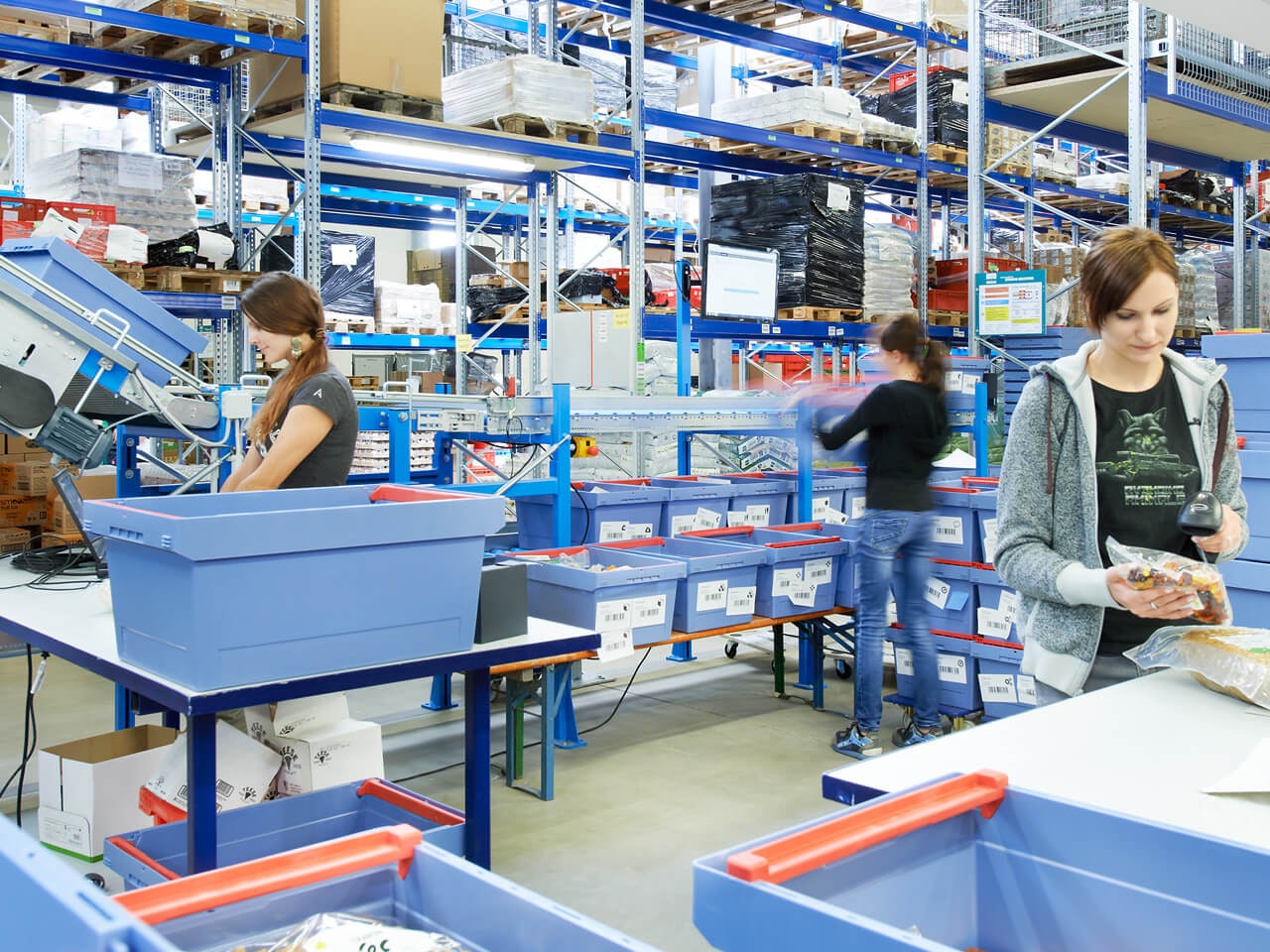 Regały paletowe i pojemniki wielokrotnego użytku MB Drei Frauen sortieren Produkte in BITO Behälter ein. Im Hintergrund sieht man ein BITO Regalsystem.