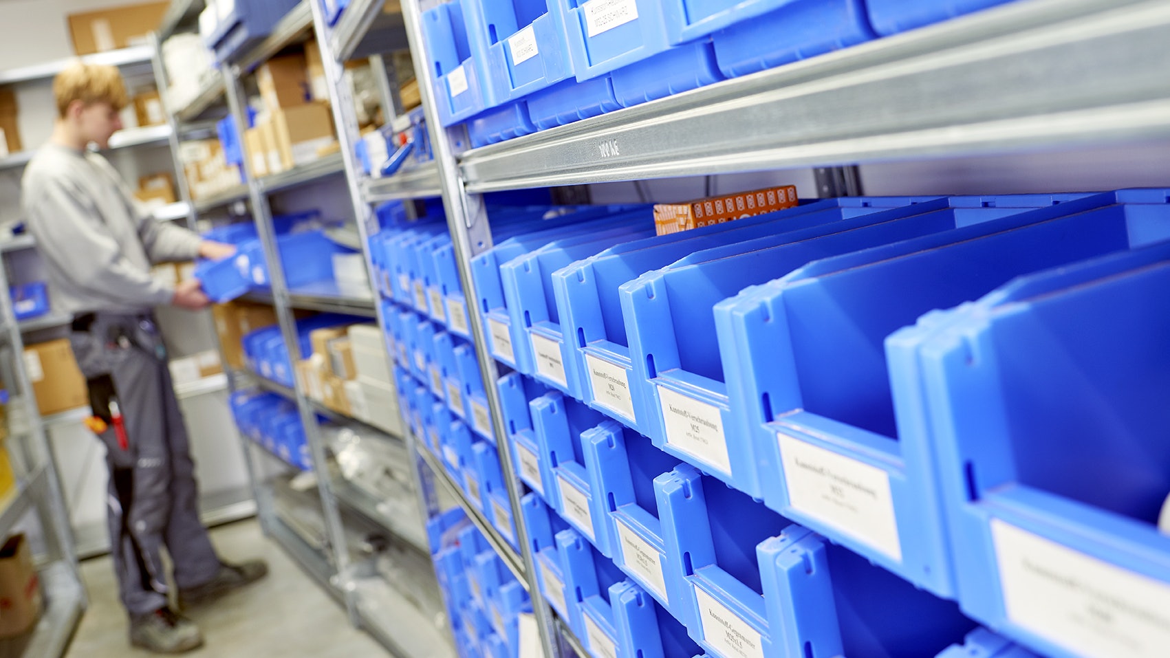 BITO Behälterregal SK Kleine BITO Behälter für die Kleinteilelagerung in einem BITO Regal. Ein Mitarbeiter sucht sich Kleinteile aus einem Behälter.