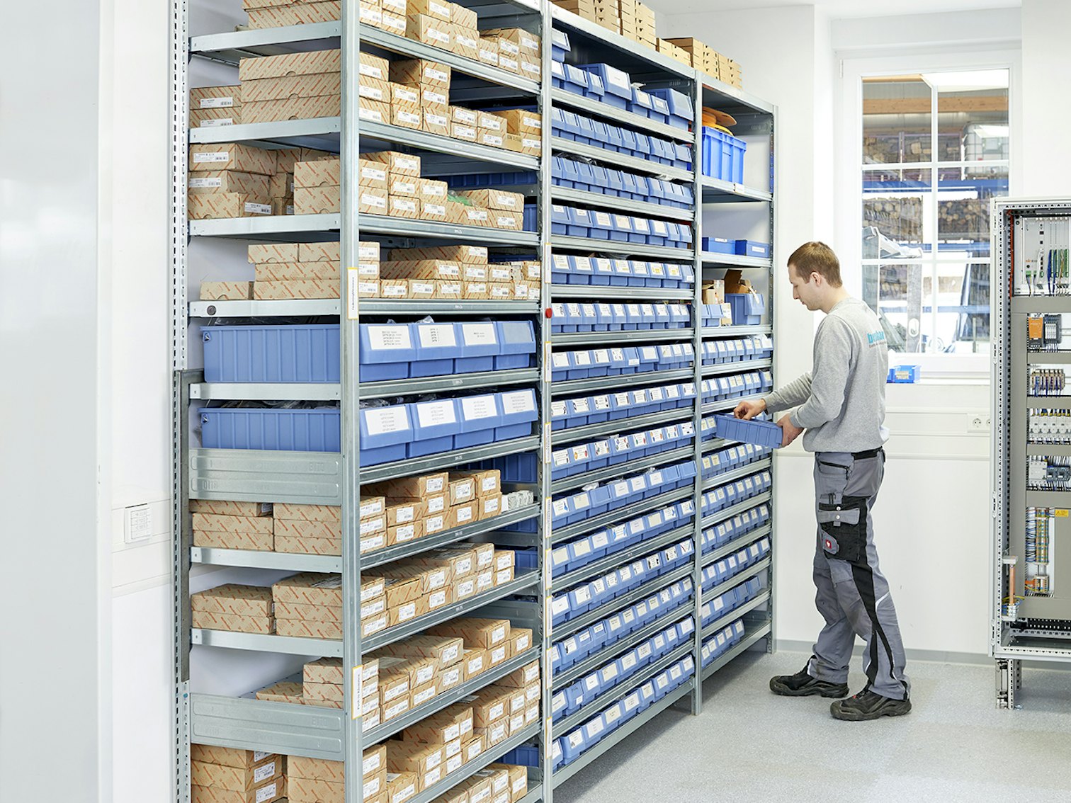 Regały z pojemnikami RK Ein Mitarbeiter der Elektro Bernhard GmbH sucht sich seine Kleinteile aus einem BITO Behälter, der in einem BITO Regal steht.