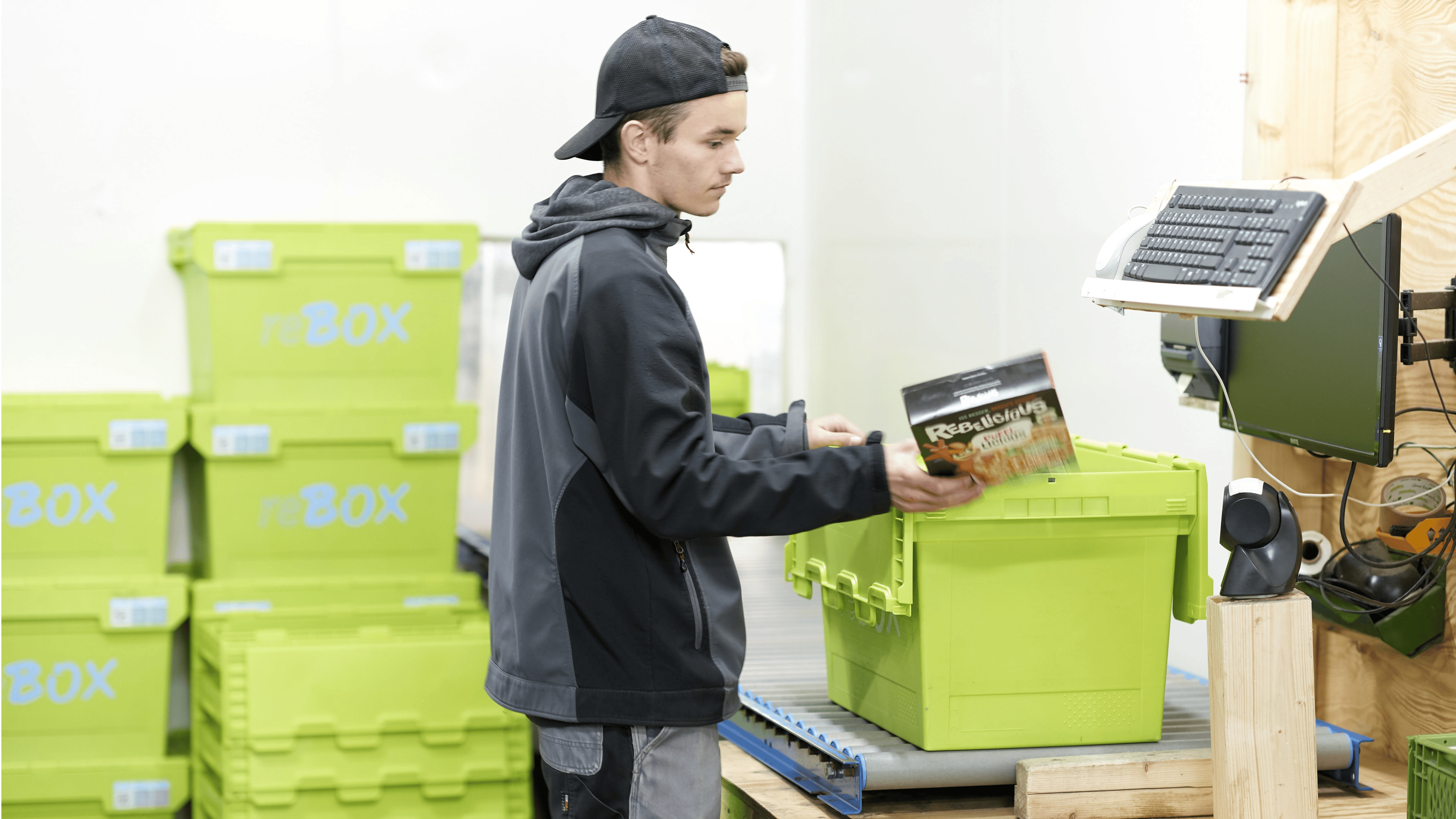 BITO MB multi-purpose containers Ein junger Mann räumt Lebensmittel aus einem BITO Behälter, der auf einem Förderband steht, aus. Im Hintergrund sind gestapelte BITO Behälter zu sehen.