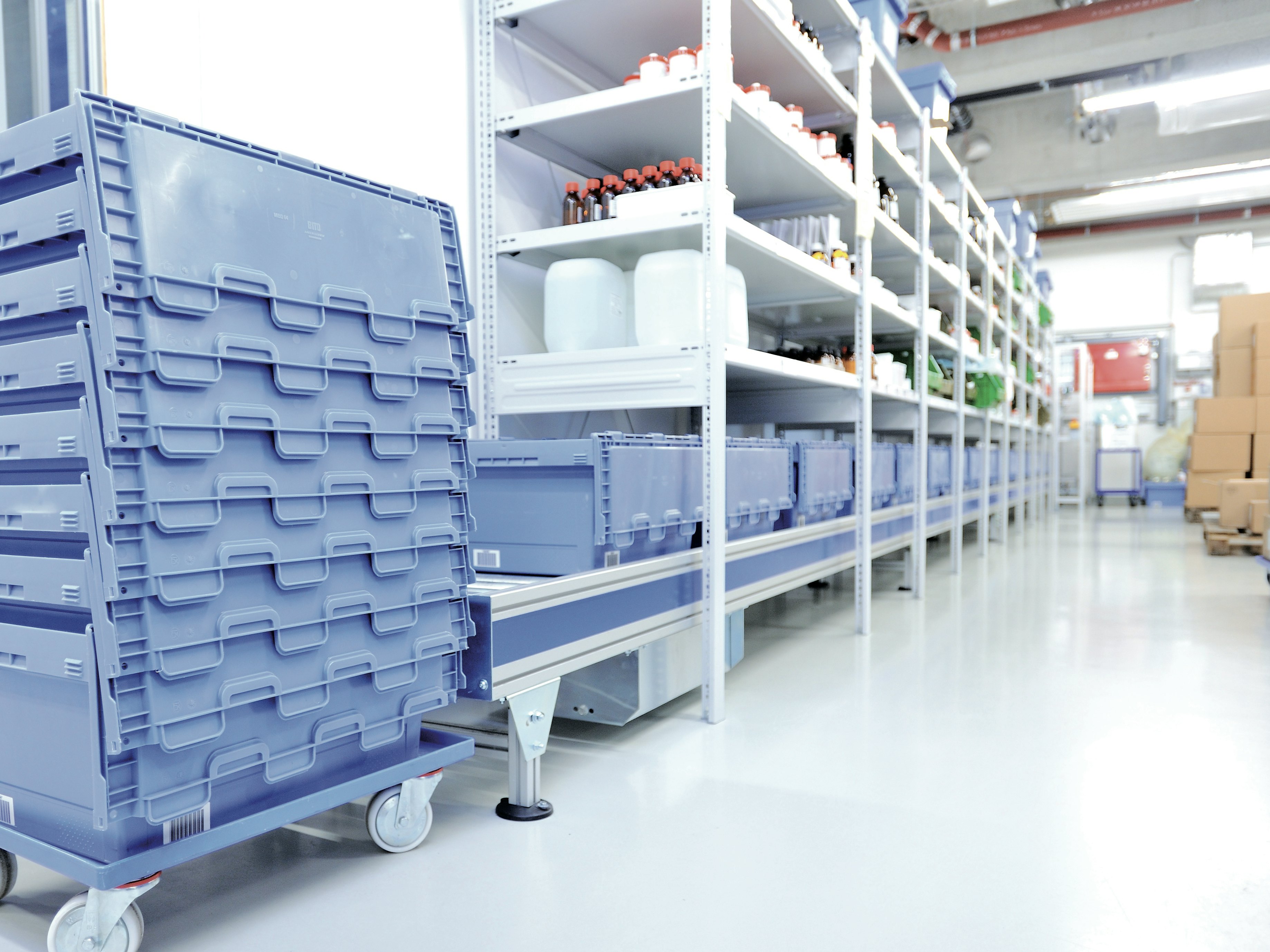 BITO genanvendelig transportkasse MB og småvarereoler Eine Rollleiste führt unter dem Medikamentenregal entlang. Auf ihr stehen BITO Behälter , die am Ende der Rollleiste gestapelt werden.