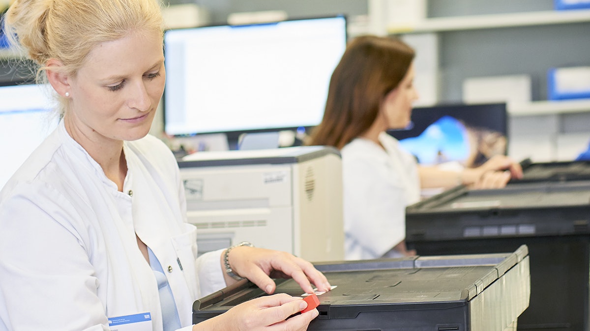 BITO Pharmabox Eine Frau im Medizinkittel schließt einen BITO Behälter, der auf Rollleisten steht.