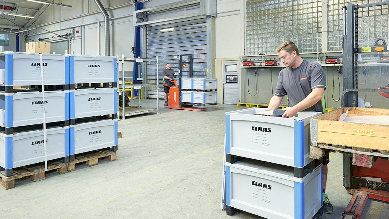 Pojemniki SL86 o dużej pojemności Ein Mitarbeiter von Claas setzt Teile aus einem BITO Behälter in eine Palette, die auf dem Stapler steht. Links davon befinden sich weitere gestapelte BITO Behälter mit der Aufschrift Claas.