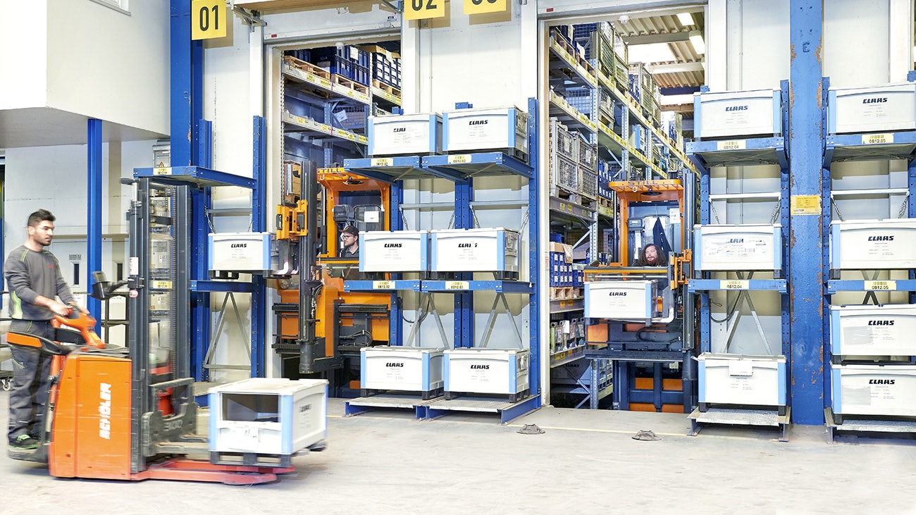 Pojemniki SL86 o dużej pojemności Stapler laden BITO Behälter mit der Aufschrift Claas in ein BITO Regal an der Wand. Im Vordergrund transportiert ebenfalls ein Stapler einem BITO Behälter.