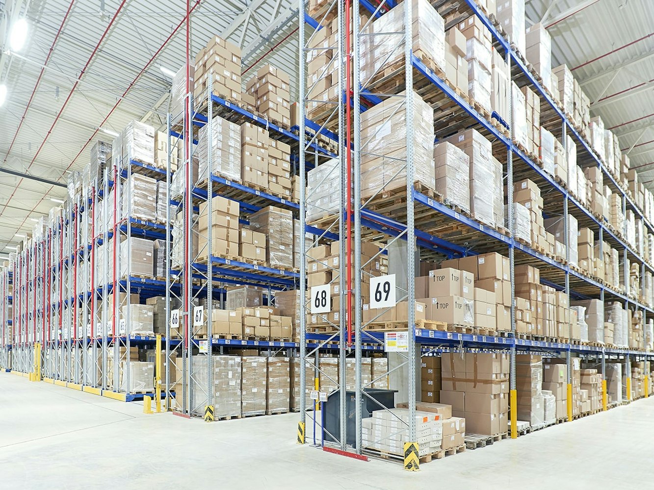BITO Mobilný paletový regál Eine große Lagerhalle in der BITO Lagerregale und Verschieberegale stehen. Diese sind gefüllt mit auf Paletten sitzenden Kartons.