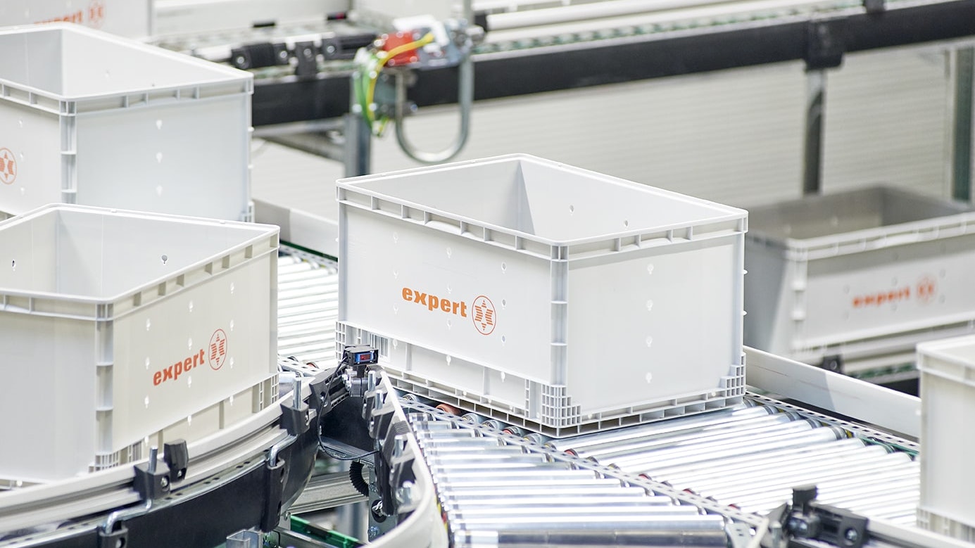 Pojemniki BITO XLmotion BITO Behälter mit der Aufschrift expert werden auf Rollleisten transportiert.