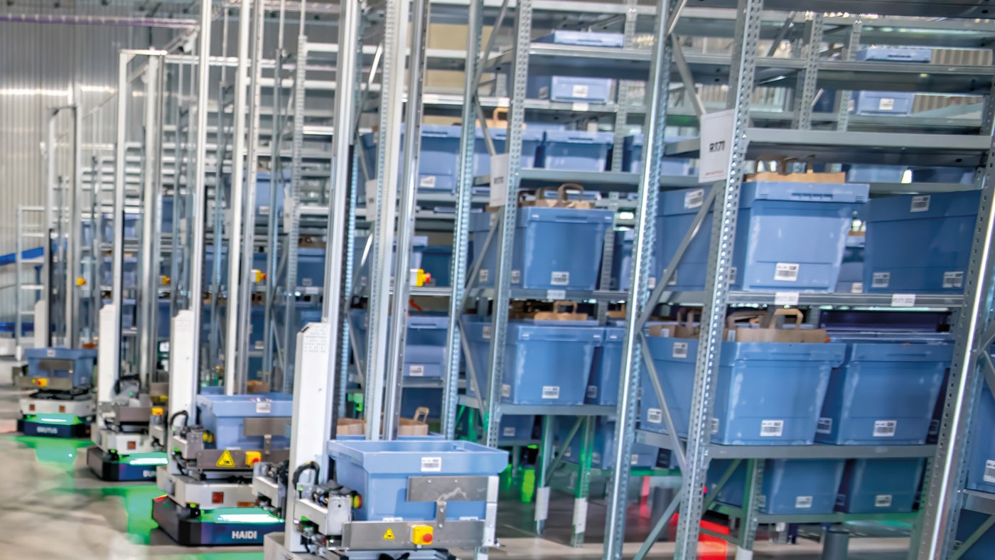 een AMR robot met magazijnbakken rijdt tussen magazijnrekken.