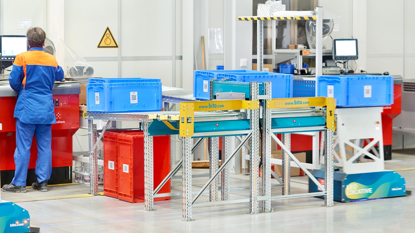 De foto toont een AGV robot en een magazijnmedewerker die samen magazijnbakken vullen.