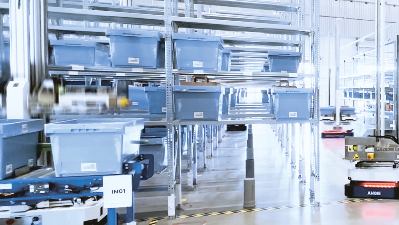 We tonen een legbordstelling vol met magazijnbakken en in de magazijngang rijdt een AMR robot rond.