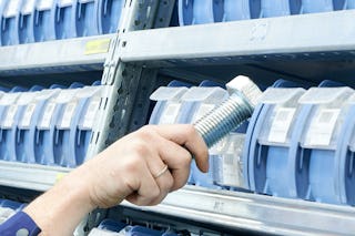 De foto toont een hand van een medewerker dat een zeer grote vijs neemt uit een bakje in een legbordstelling