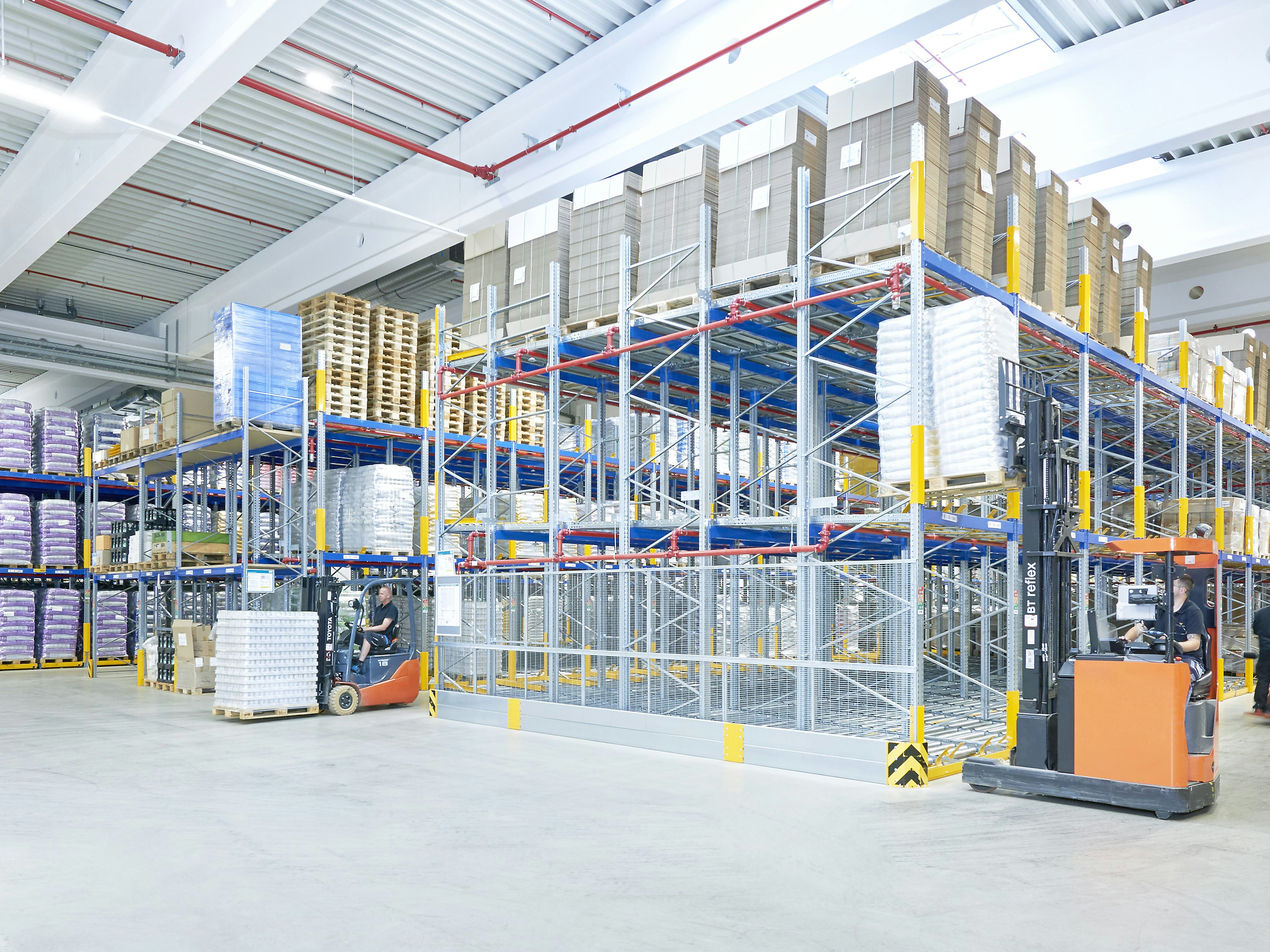 Mehrere Arbeiter mit Flurförderzeugen in einem Palettenregal-Lager Mehrere Arbeiter mit Flurförderzeugen in einem Palettenregal-Lager