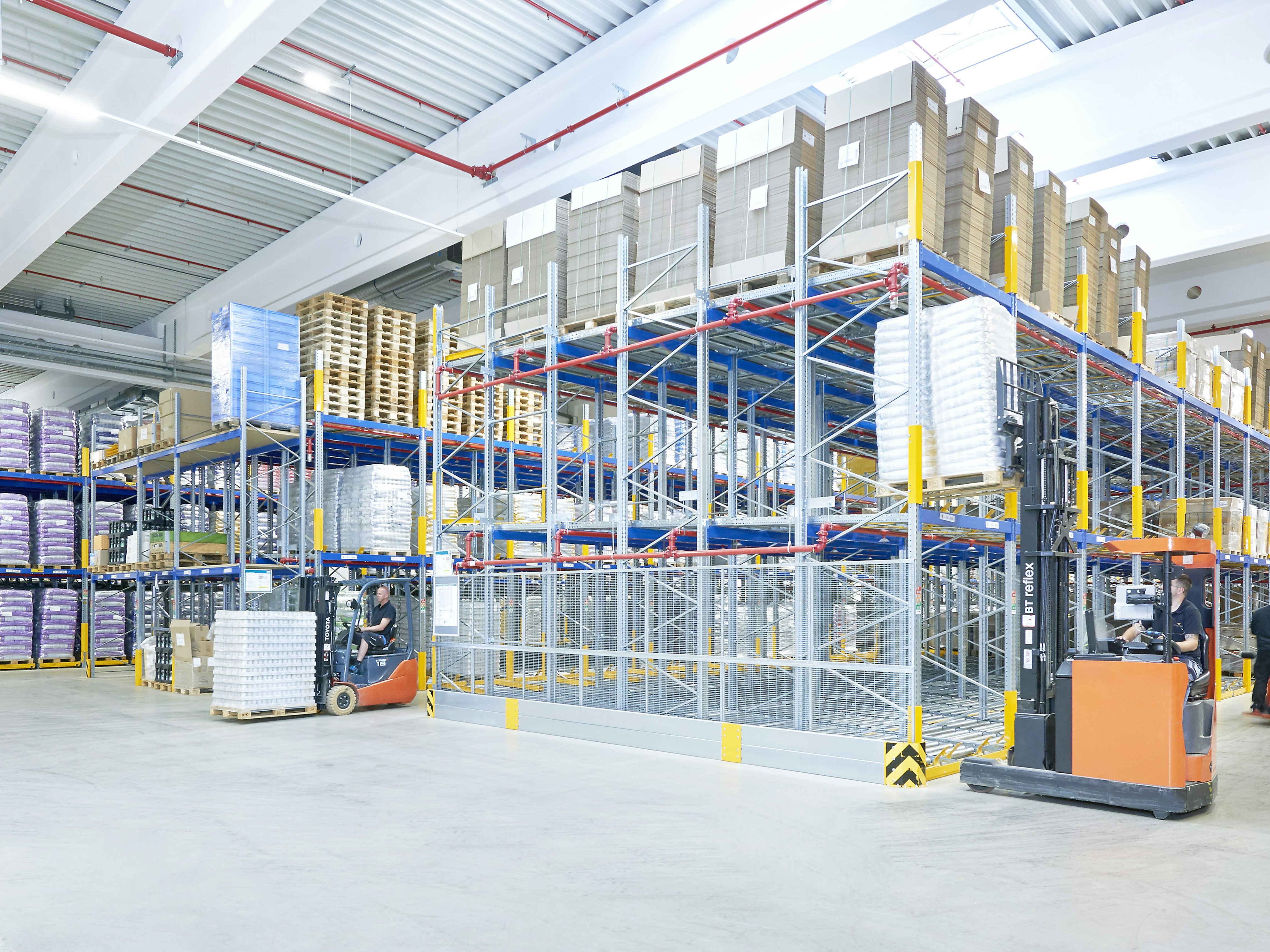 Mehrere Arbeiter mit Flurförderzeugen in einem Palettenregal-Lager Mehrere Arbeiter mit Flurförderzeugen in einem Palettenregal-Lager