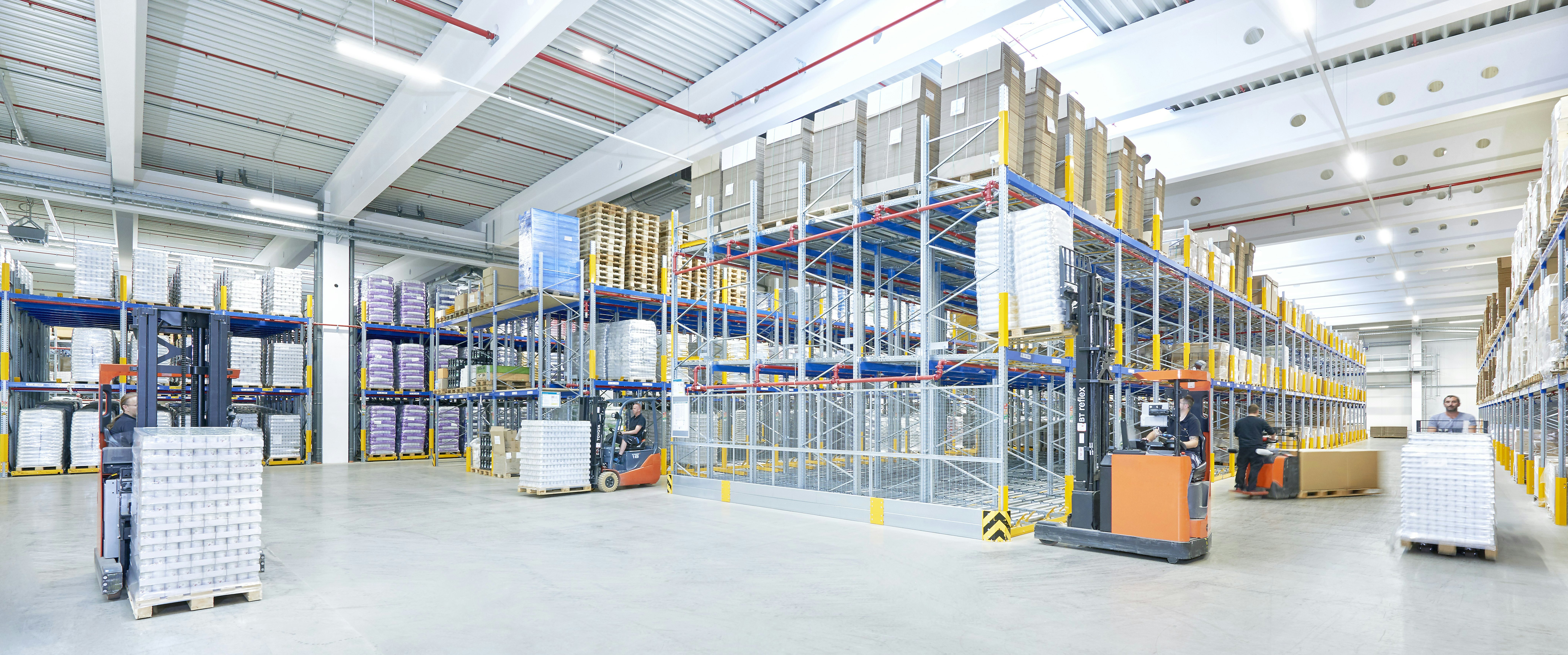 Mehrere Arbeiter mit Flurförderzeugen in einem Palettenregal-Lager Mehrere Arbeiter mit Flurförderzeugen in einem Palettenregal-Lager